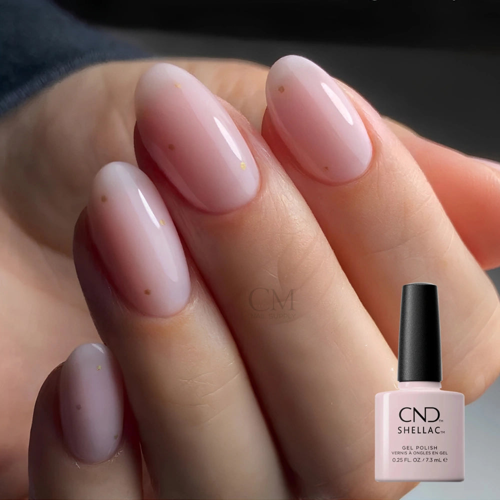 A close-up of a hand with glossy, pale pink manicured nails, alongside a bottle of CND Shellac backyard nuptials gel nail polish in the matching shade.