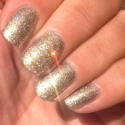A close-up of a hand with manicured nails painted in a sparkling gold glitter nail polish, reflecting bright light CND Shellac Locket Love gel nail polish