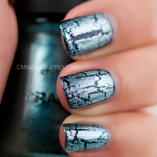 Close-up of a hand with fingernails painted in a metallic teal-blue shade with a black crackle pattern, with a matching nail polish bottle blurred in the background. A watermark reads CMNAILSSUPPLY. China Glaze Crackle Nail Polish #1047 Oxidized Aqua