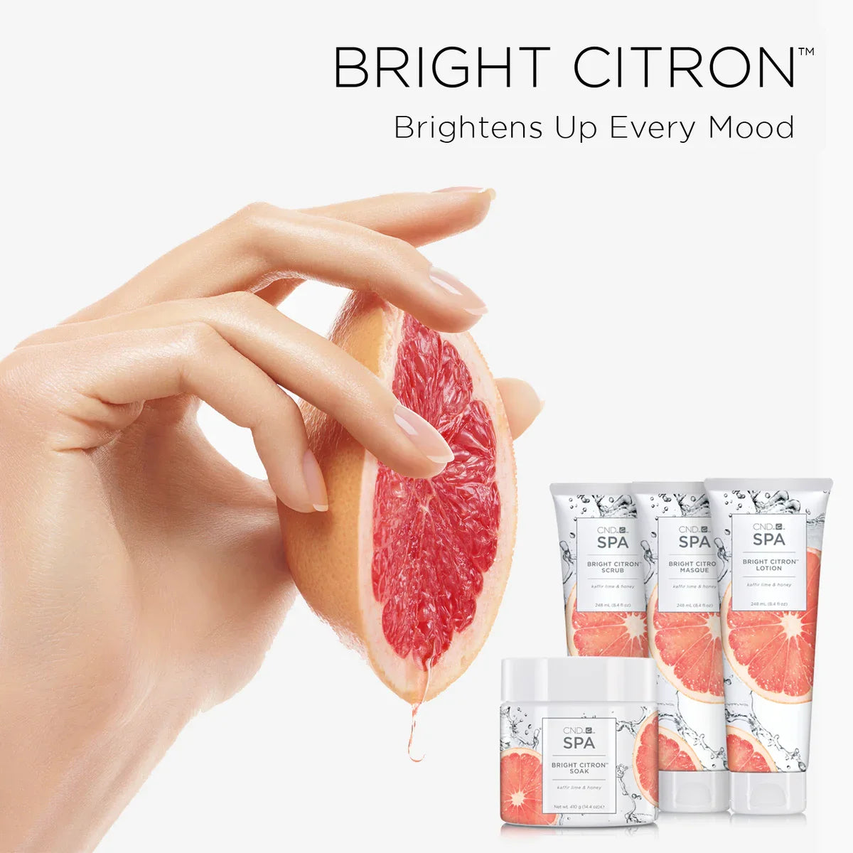 Hand holding a sliced grapefruit with skincare products labeled 'Bright Citron' on a white background