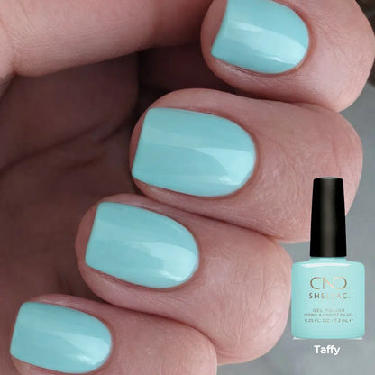 A close-up of a hand with fingernails painted in a glossy light aqua shade, with a bottle of CND Shellac nail polish labeled 'Taffy' shown at the lower right.