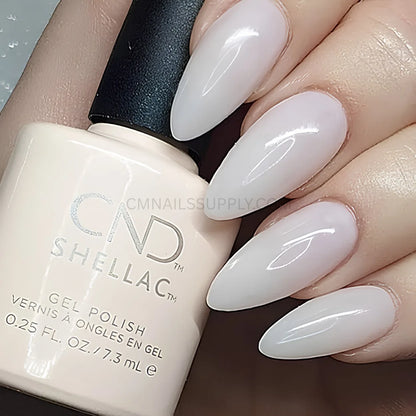 A close-up of a hand with long, glossy almond-shaped nails painted in a very pale pinkish-white gel polish, holding a bottle of CND Shellac Gel Polish Bouquet
