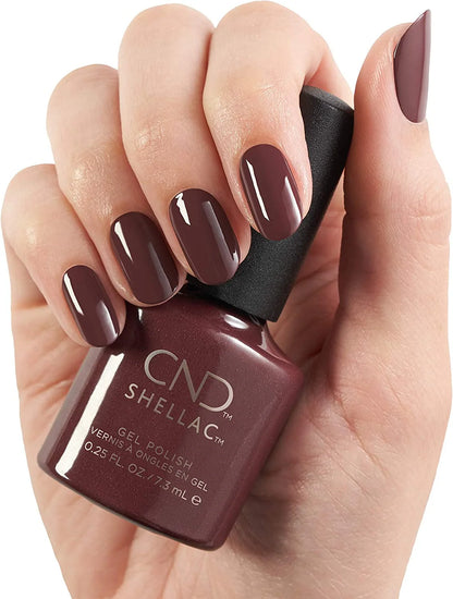 A hand holding a bottle of CND Shellac Arrowhead gel nail polish in a deep plum-brown shade, with the nails painted to match against a clean white background.