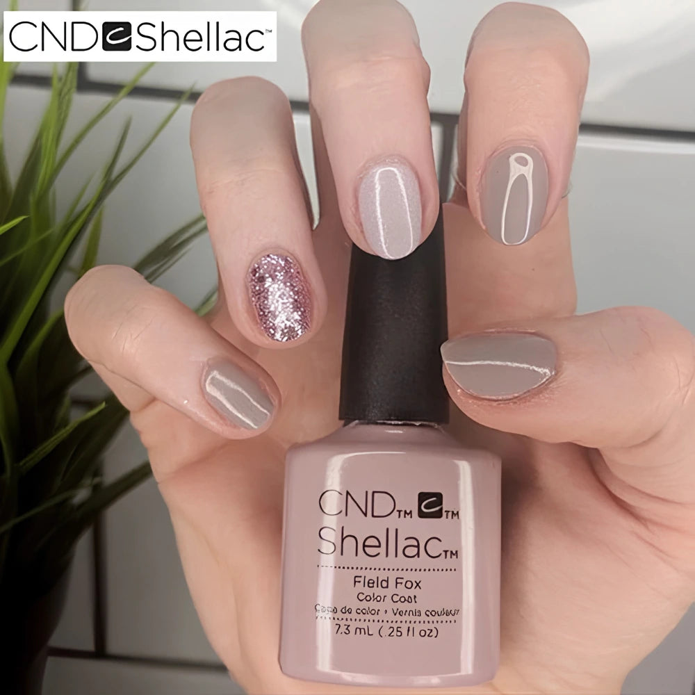 Hand holding a bottle of CND Shellac 'Field Fox' with a neutral nail design.
