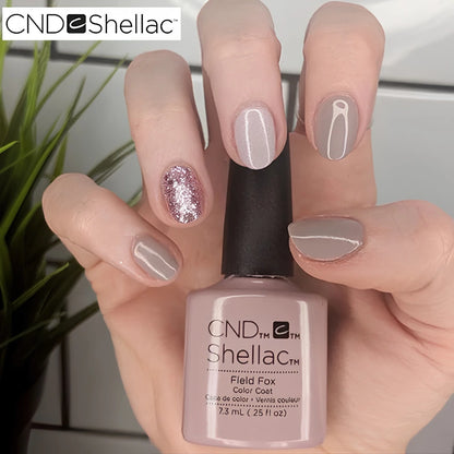 Hand holding a bottle of CND Shellac 'Field Fox' with a neutral nail design.