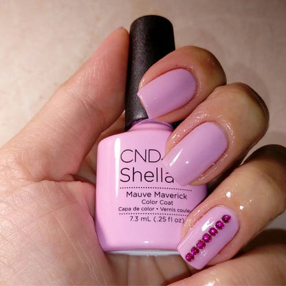 A hand holding a bottle of CND Shellac Mauve Maverick Color Coat nail polish, showing the light pink polish applied to the fingernails.