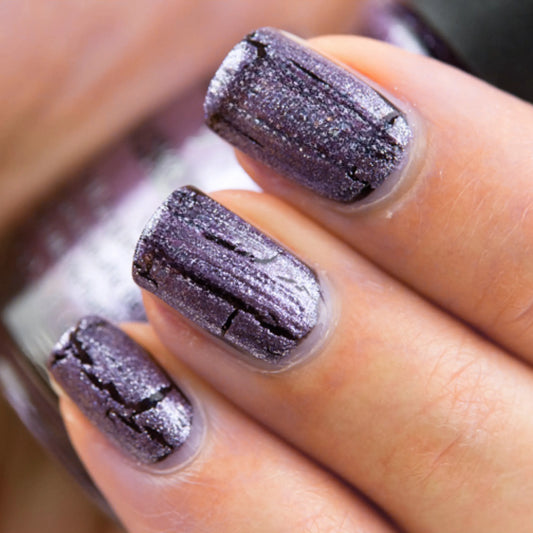 A close-up of a hand with manicured nails painted in a shimmery metallic plum-purple China Glaze Crackle 1045 Latticed Lilac nail polish