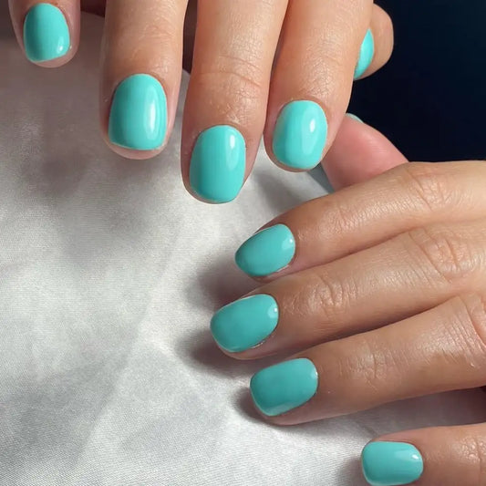 Close-up of manicured fingernails painted in DC Nile Green #033 a solid light aqua/turquoise shade, resting on a white textured fabric surface.