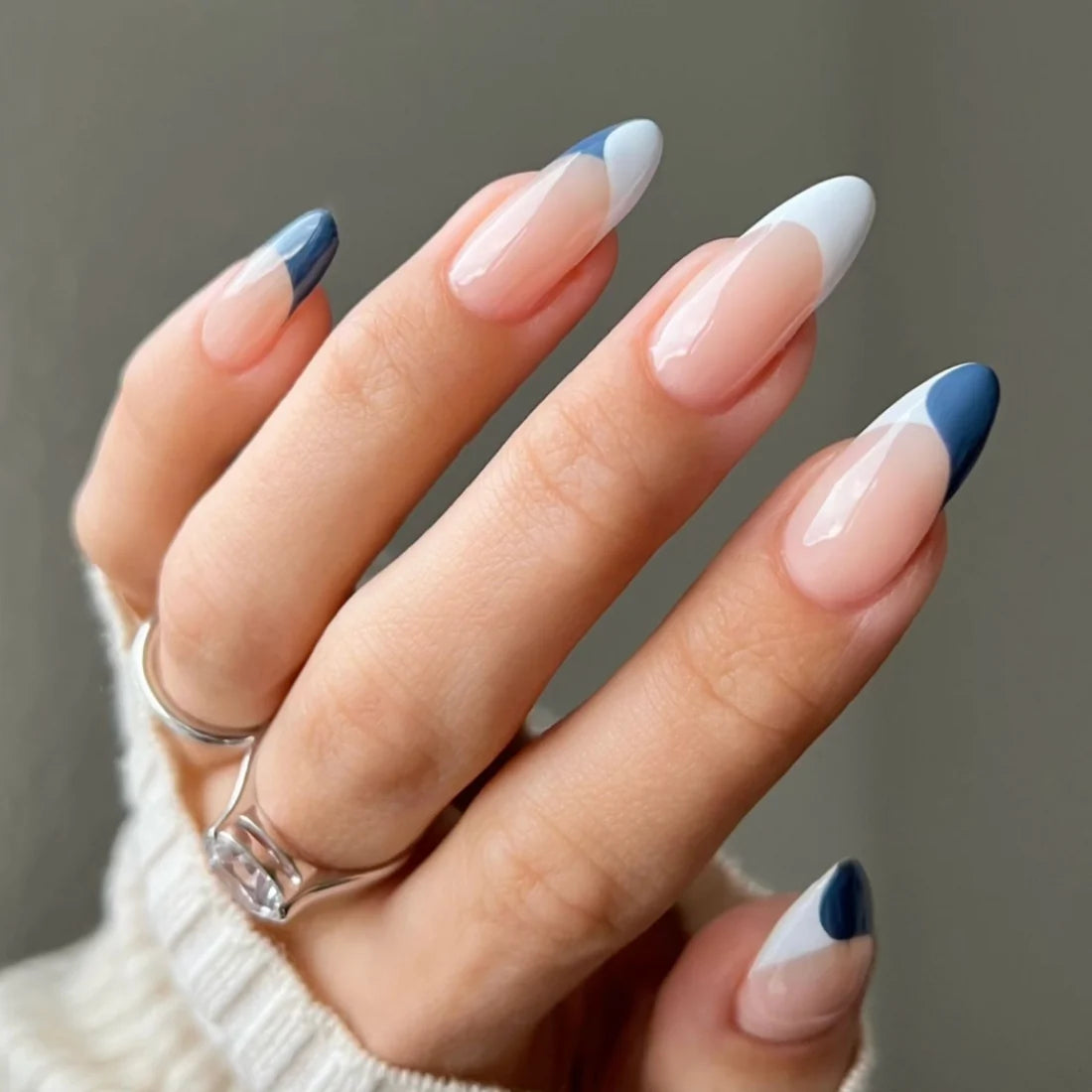 Hand with nail art painted in a design of white, blue, and beige on a neutral background