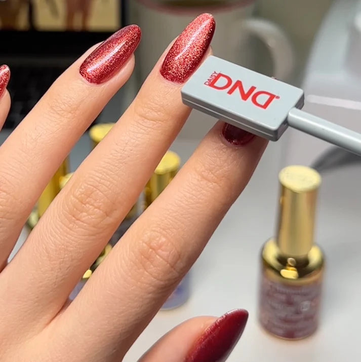 Hand with red glittery nails holding a DND cat eye magnet, with a bottle in the background.