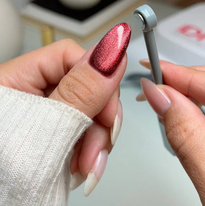 Hand with red glittery nail polish holding a DND cat eye magnet for cat eye polish