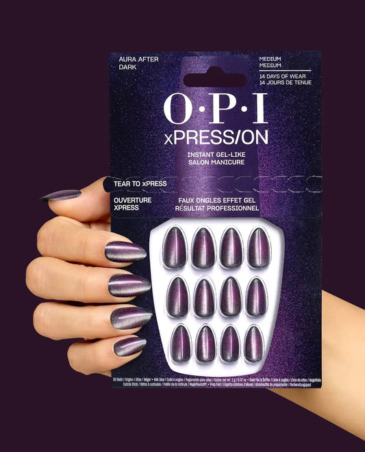 A hand holding an OPI xPressOn instant gel-like press-on nail set against a dark purple background. The nails are metallic and shimmer with a deep plum and silver coloration.