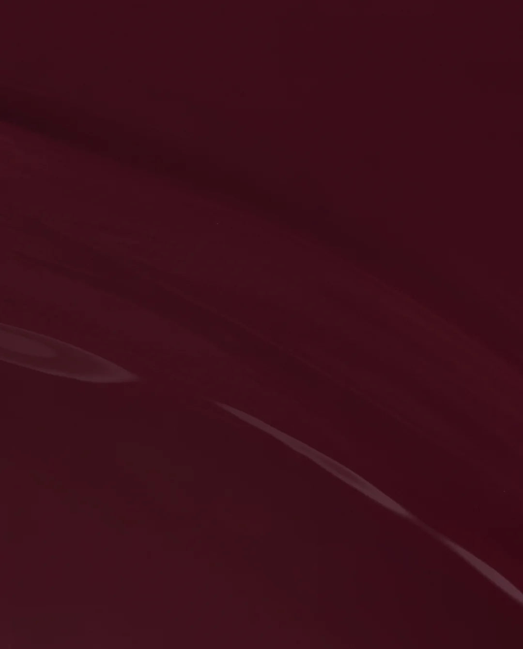 A close-up of a glossy deep burgundy or maroon surface with soft light reflections.