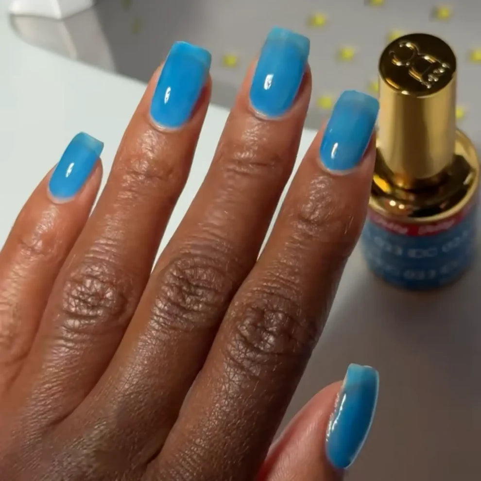 Manicured hand with dark skin tone wearing DC Jelly 023 Capri jelly gel polish in a bright azure blue finish