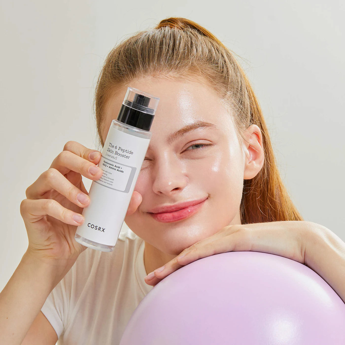 Woman holding a Front view of the COSRX 6 Peptide Skin Booster Serum bottle showing the 150ml label skincare product against a plain background