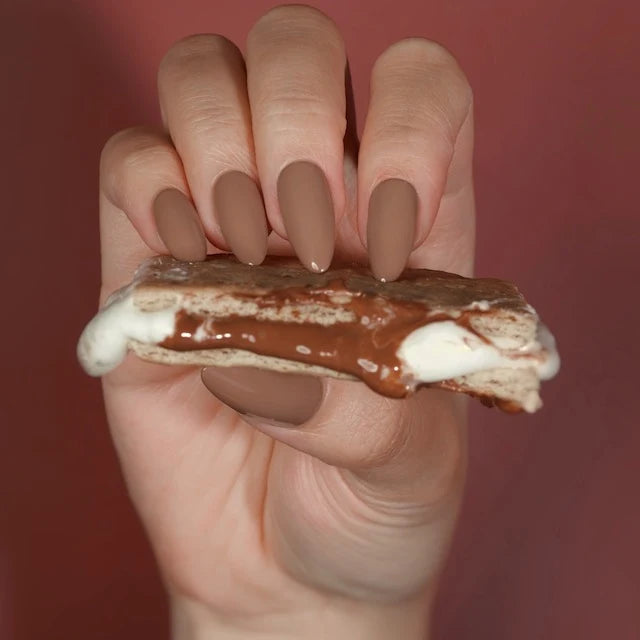 Creamy brown neutral creme gel polish, DND DC S’Mores #316, shown on a nails holding smores