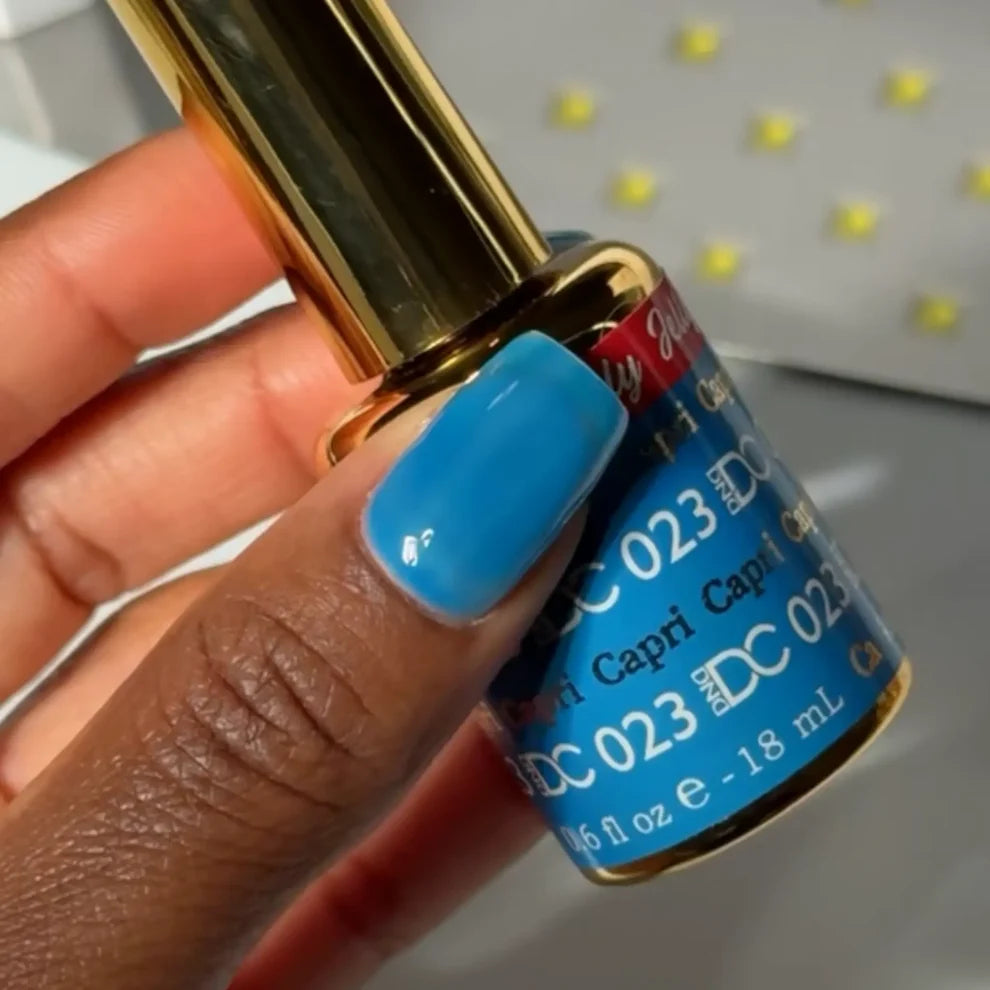 Hand holding a bottle of DC 023 nail polish with blue cap and gold accents.