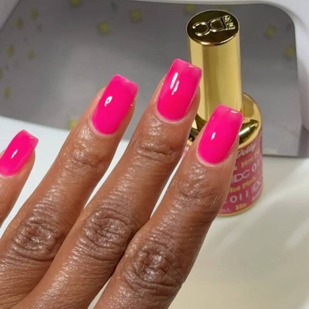 Deep skin tone manicured hand showing DC Jelly 011 Hot Pink jelly gel polish with a bright creamy finish