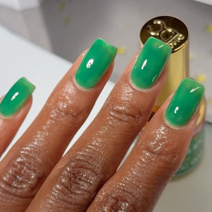 Hand with a fresh manicure holding the DC Jelly Kelly jelly gel polish bottle to show the label and shade