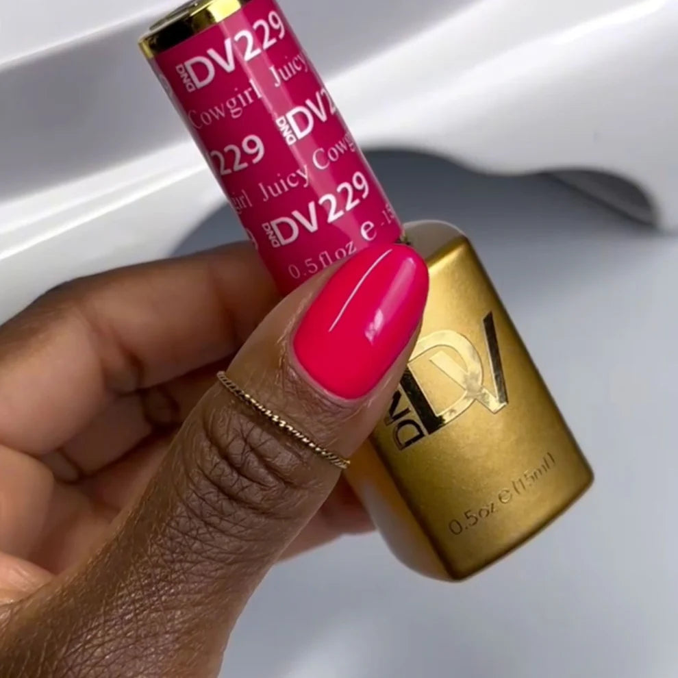 Hand holding a pink lip gloss with gold cap, brand 'DV229' visible