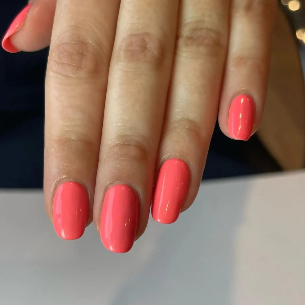 Close up manicure shot of DND Coral Reef #556 on the nail, highlighting the vibrant coral finish and pink undertone