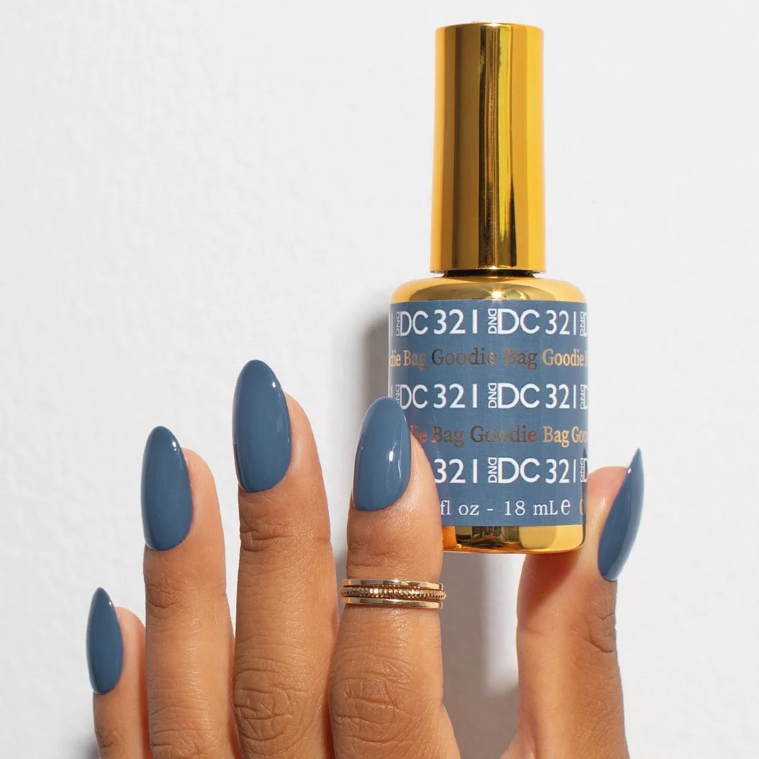 Close up of a hand holding a DND DC Goodie Bag #321 manicure with a glossy denim blue finish