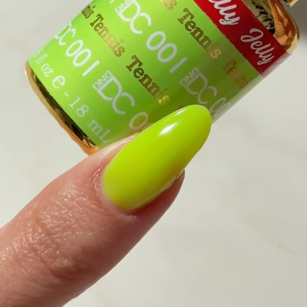 A close-up of a fingernail painted in a bright neon yellow-green gel polish, with a bottle labeled DND DC Jelly Gel 001 Tennis Jelly held behind the finger.