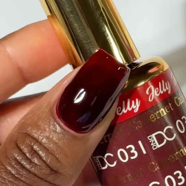 DND DC manicured hand holding the jelly nail polish bottle for Cabernet 031, showcasing the wine red color on the nails