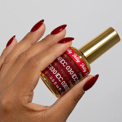 DND DC manicured hand holding the jelly nail polish bottle for Sangria 030, showcasing the deep red berry color on the nails