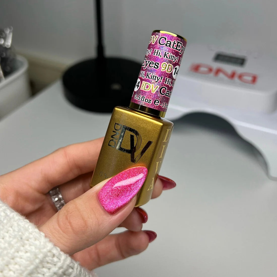 Hand with a hot pink cat eye manicure holding the DND Diva Cat Eye Gel Polish #14 Hi Kitty bottle.