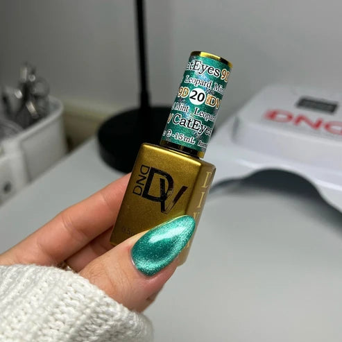 Hand with a turquoise mint cat eye manicure holding the DND Diva Cat Eye Gel Polish #20 Leopard Mint bottle.