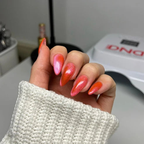Hand with a watermelon pink cat eye manicure holding the DND Diva Cat Eye Gel Polish #22 Jelly Belly Rubs bottle.