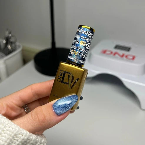 Hand with a velvety blue cat eye manicure holding the DND Diva Cat Eye Gel Polish #23 Catnip Craze bottle.