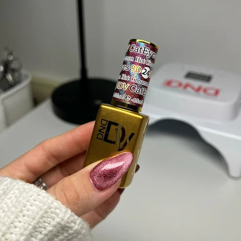 Hand with a cinnamon pink cat eye manicure holding the DND Diva Cat Eye Gel Polish #24 Hot Cinnamon bottle.