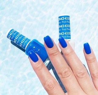 A hand with bright royal blue painted nails holds a bottle of nail polish against a light blue water-textured background. The bottle label shows the brand name 'DND' and shade number '433'.