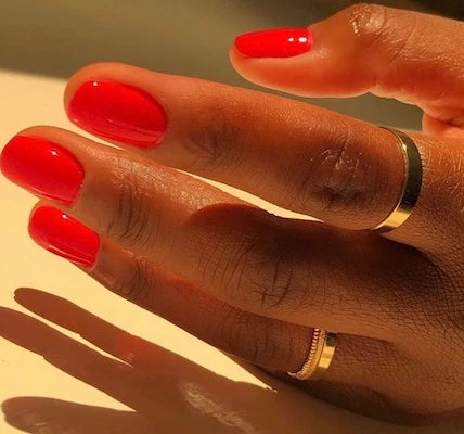Hand wearing DND Red #563 gel polish, showing the classic neon red tone on the nails