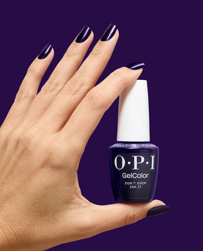 Hand with dark nail polish holding a bottle of OPI GelColor don't over ink it gel nail polish against a purple background