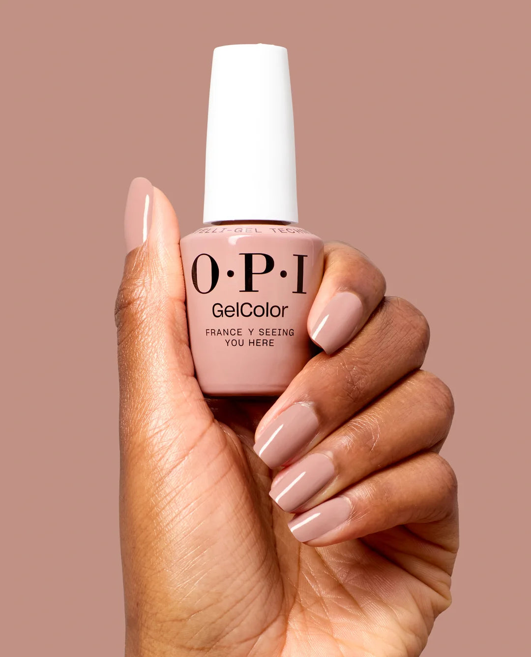 Hand holding a bottle of OPI Gel Color - France-y Seeing You Here Gel Polish F039 nail polish with matching nails against a brown background