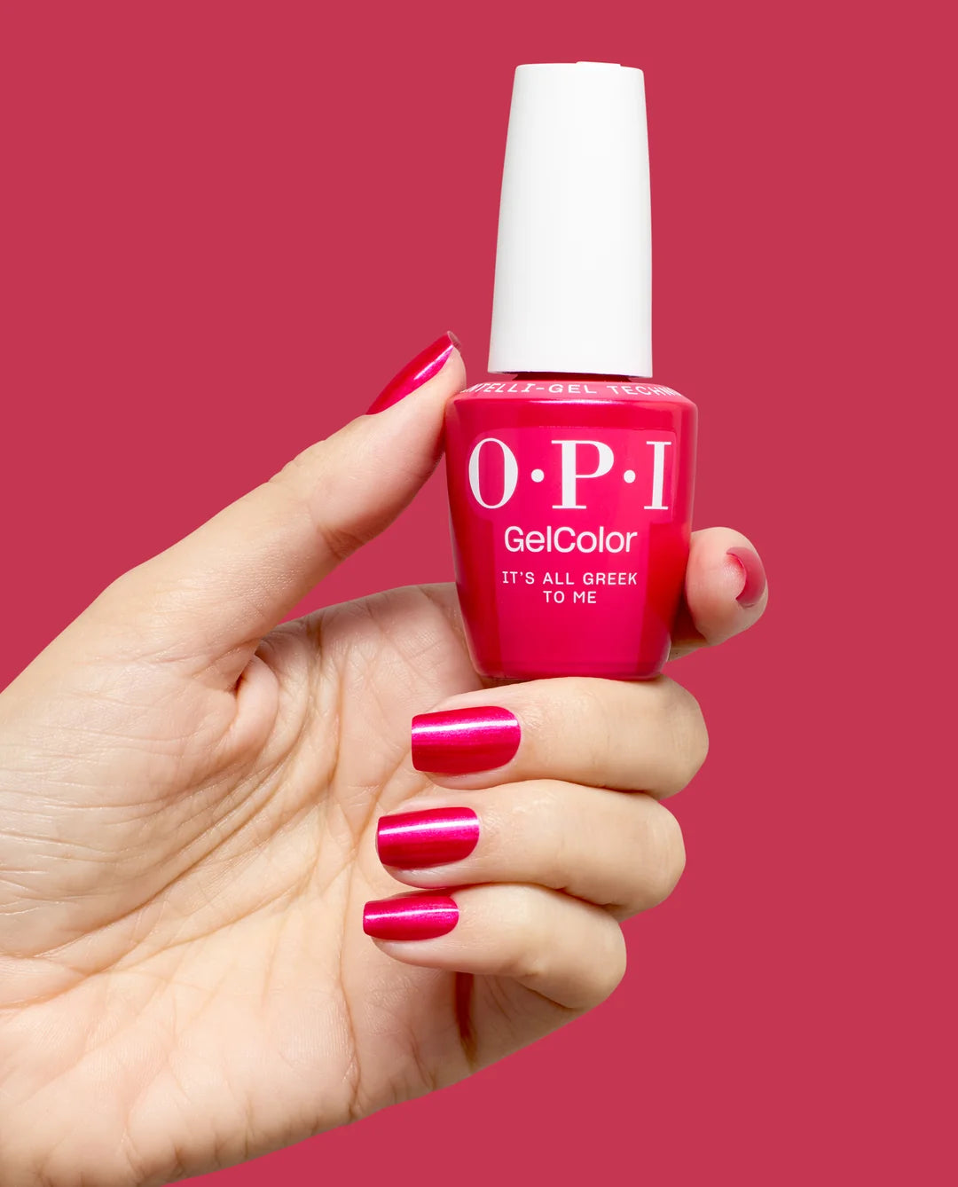 Hand holding a bottle of OPI GelColor its all greek to me gel nail polish with matching pink nails against a red background