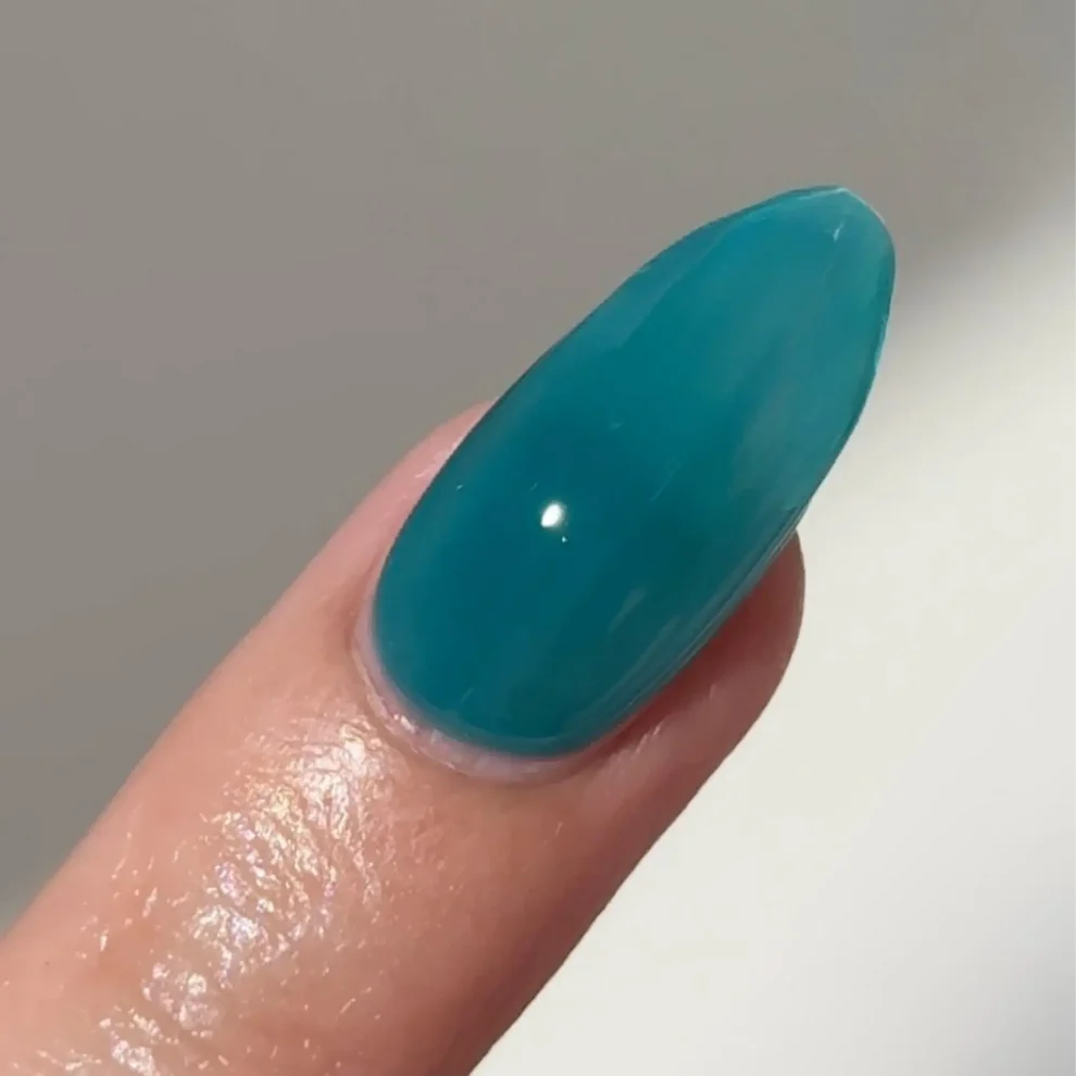 Manicured hand with light skin tone wearing DC Jelly 024 Jade jelly gel polish in a turquoise green blue finish