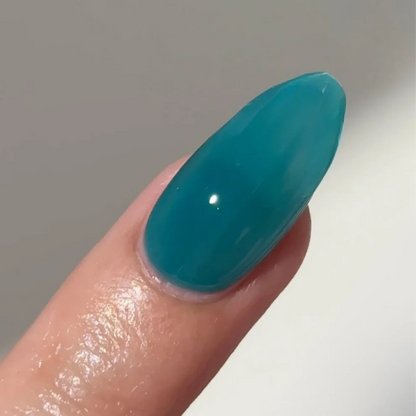 Manicured hand with light skin tone wearing DC Jelly 024 Jade jelly gel polish in a turquoise green blue finish