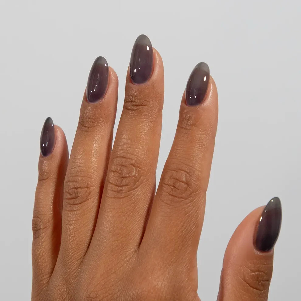 Deep skin tone manicured hand showing DC Jelly 027 Coal jelly gel polish with a moody smoky grey glow
