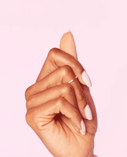 A close-up of a hand with long, almond-shaped pink OPI Let me Bayou a Drink manicured nails, wearing a delicate silver ring on one finger, set against a solid light pink background.