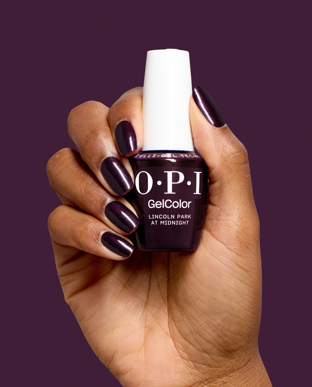 Hand holding a bottle of OPI GelColor Lincoln Park at Midnight gel polish with a dark purple color on a matching background