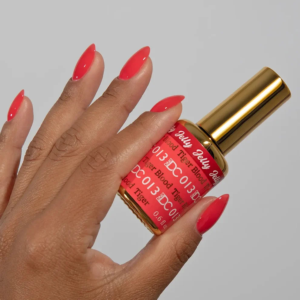 Manicured hand holding the DC Jelly 013 Tiger Blood jelly nail polish bottle, showcasing the fiery orange red color on the nails
