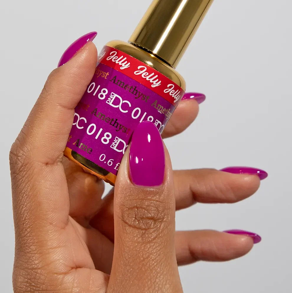Manicured hand holding the DC Jelly 018 Amethyst jelly nail polish bottle, showcasing the magenta purple color on the nails