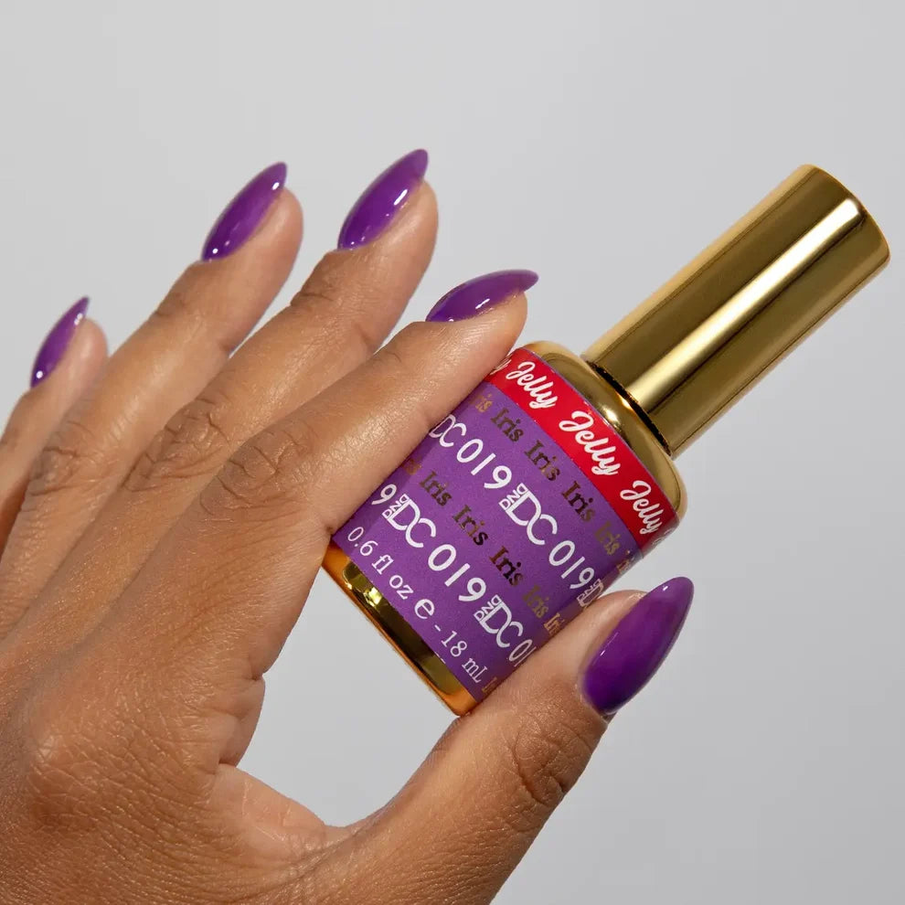 Manicured hand holding the DC Jelly 019 Iris jelly nail polish bottle, showcasing the light purple color on the nails