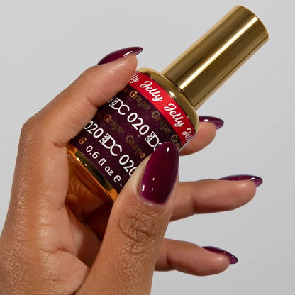 Manicured hand holding the DC Jelly 020 Grape jelly nail polish bottle, showcasing the warm purple color on the nails