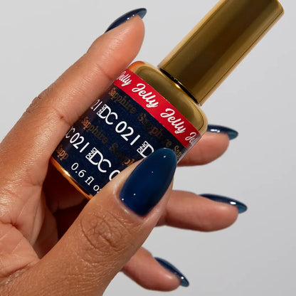 Manicured hand holding the DC Jelly 021 Sapphire jelly nail polish bottle, showcasing the deep teal blue color on the nails