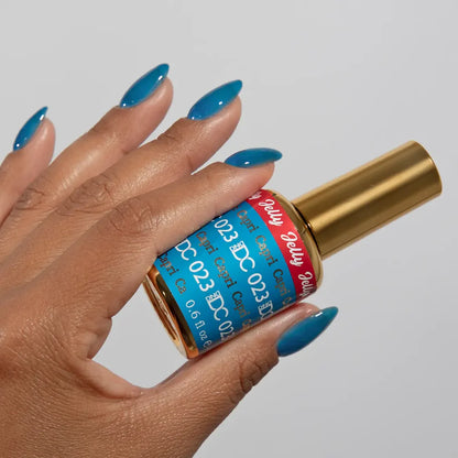 Manicured hand holding the DC Jelly 023 Capri jelly nail polish bottle, showcasing the bright azure blue color on the nails